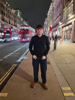 Two red double-decker buses and a black taxi on Regent Street at night, with Diego standing on the pavement in a dark polo and trousers.
