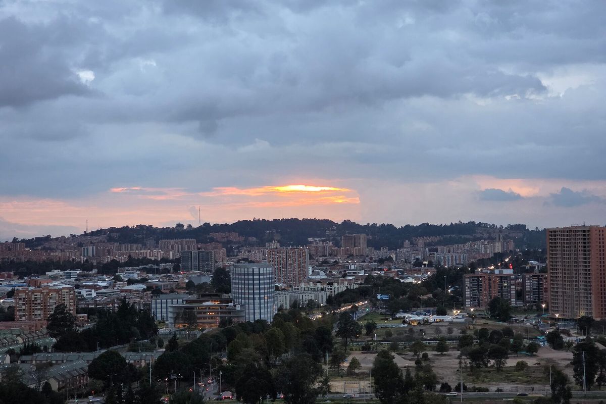 Wide dusk view over northern Bogotá from a hillside in La Calera, with dark clouds and an orange glow near the horizon.